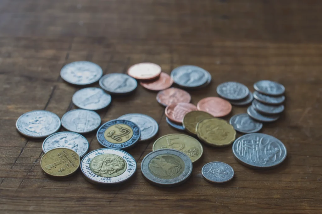 assorted international coins of various sizes and metals scattered on a wooden surface